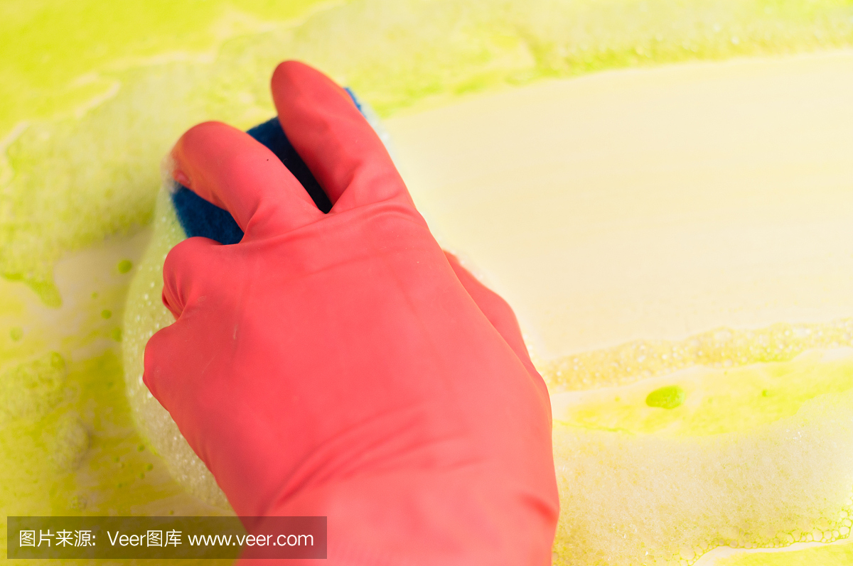 男人或女人的手戴着红色橡胶手套,用蓝色海绵擦拭脏桌子